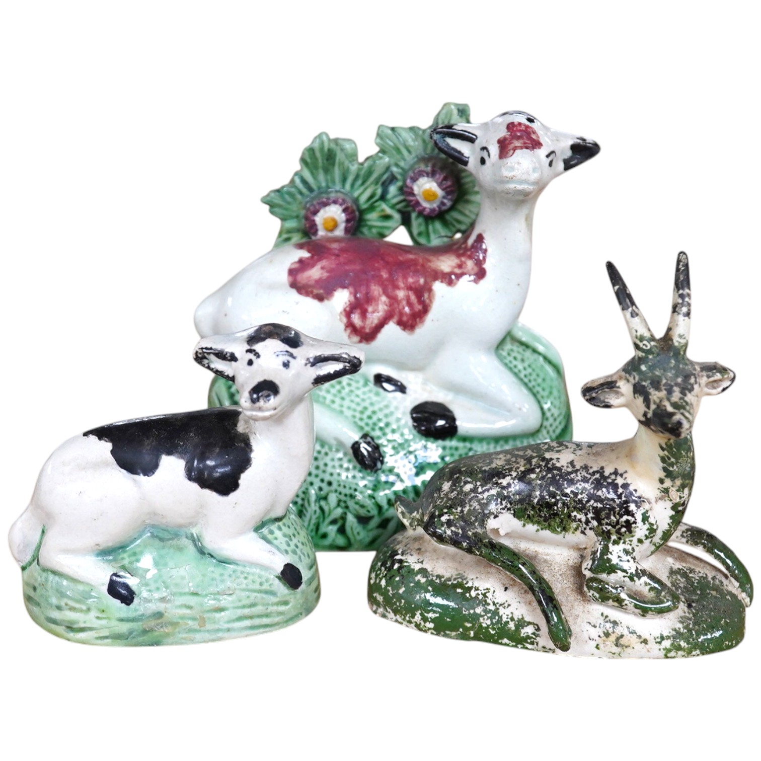 Two late 18th century Staffordshire coloured creamware figures of recumbent cows and a spongeware deer, largest 10cm wide (3). Condition - restored